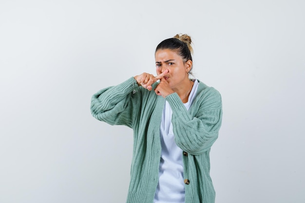 Mujer joven con camisa blanca y chaqueta de punto verde menta mostrando gesto x y mirando acosado