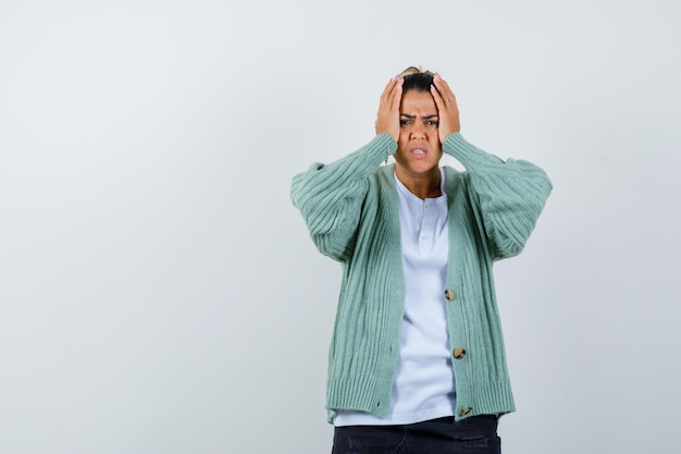 Foto gratuita mujer joven con camisa blanca y chaqueta de punto verde menta tomados de la mano a la cabeza y mirando molesto