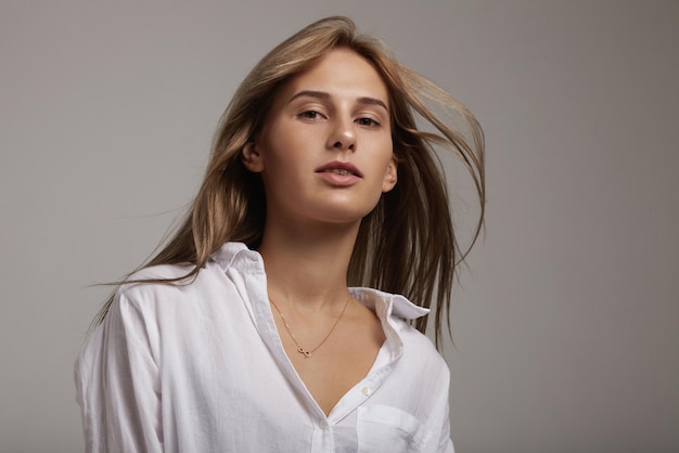 Mujer joven con camisa blanca mirando a la cámara cabello lacio soplado por el viento