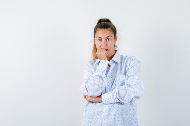 Mujer joven con camisa blanca mordiendo el puño emocionalmente y mirando ansioso