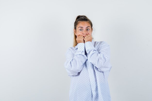 Mujer joven con camisa blanca mordiendo los puños y mirando sorprendido