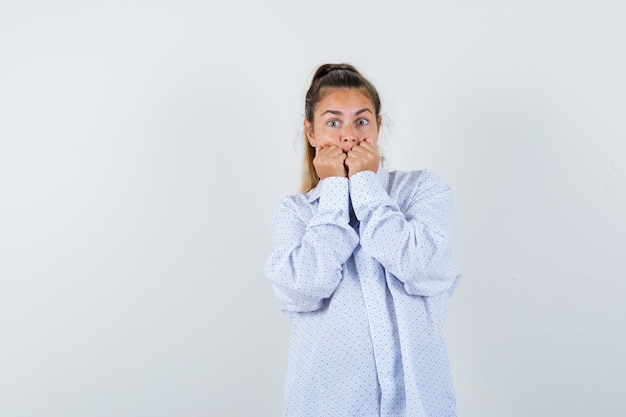 Mujer joven con camisa blanca mordiendo los puños y mirando sorprendido