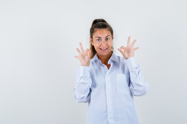 Mujer joven con camisa blanca mostrando signos de ok y mirando feliz