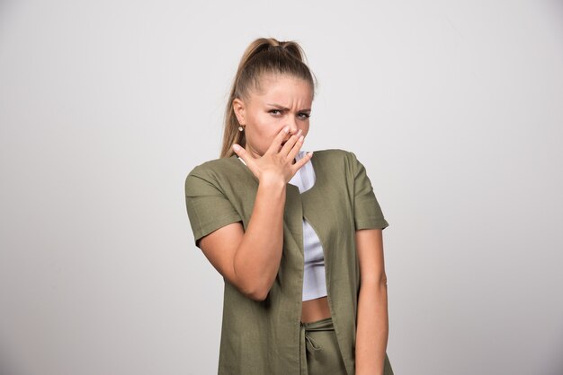 Mujer joven con camisa blanca que se siente enojada en la pared gris.