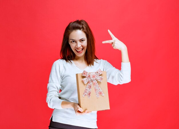 Mujer joven con camisa blanca sosteniendo una caja de regalo de cartón y mostrando un signo de mano positivo