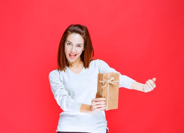 Mujer joven con camisa blanca sosteniendo una caja de regalo de cartón y mostrando un signo de mano positivo