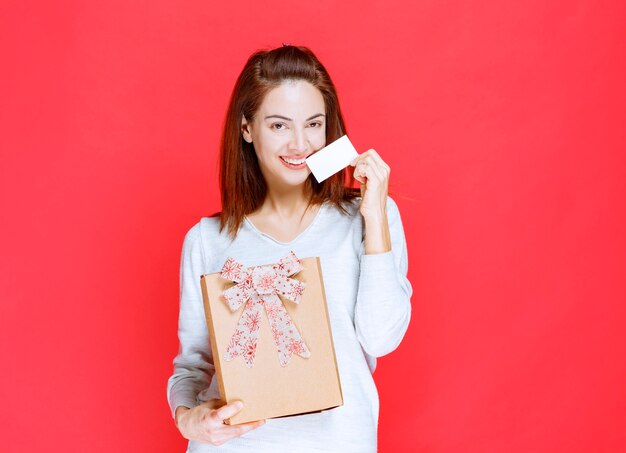 Mujer joven con camisa blanca sosteniendo una caja de regalo de cartón y presentando su tarjeta de visita