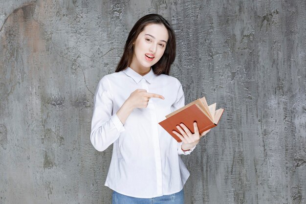 Mujer joven con camisa blanca sosteniendo un libro para su clase y señalando. foto de alta calidad
