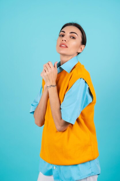 Mujer joven con una camisa y un chaleco naranja sobre un fondo turquesa mira a la cámara con una leve sonrisa de confianza