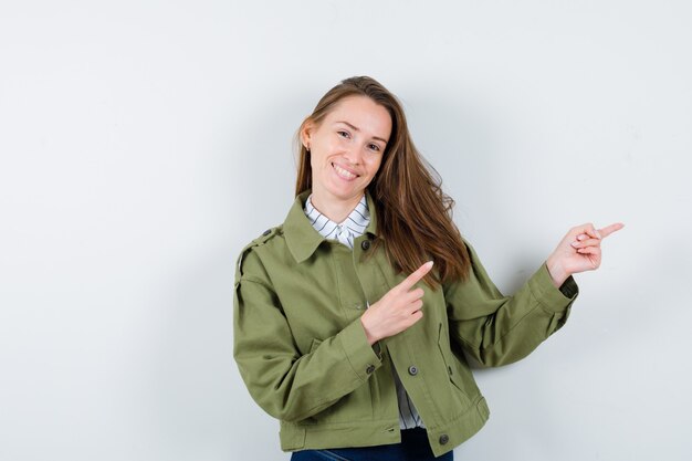 Mujer joven en camisa, chaqueta apuntando hacia el lado derecho y mirando alegre, vista frontal.