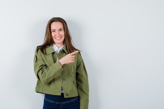 Foto gratuita mujer joven en camisa, chaqueta apuntando a un lado y mirando alegre, vista frontal.