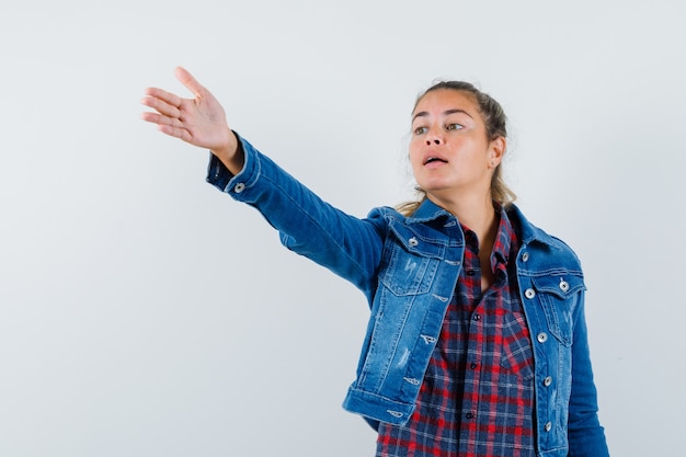 Foto gratuita mujer joven en camisa, chaqueta estirando la mano para dar instrucciones y mirando confiada, vista frontal.