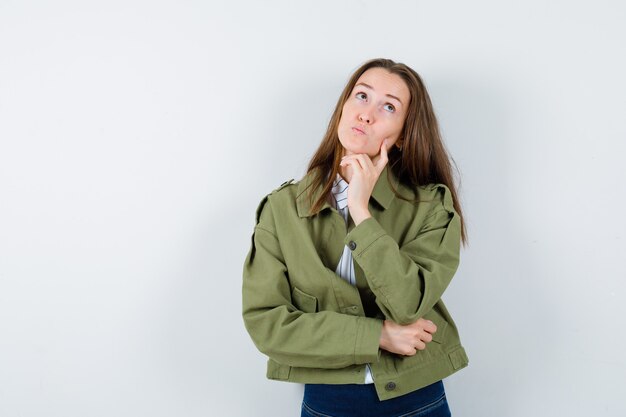 Mujer joven en camisa, chaqueta mirando hacia arriba y mirando pensativo, vista frontal.