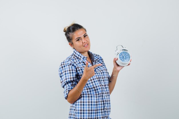 Mujer joven en camisa a cuadros apuntando al reloj.