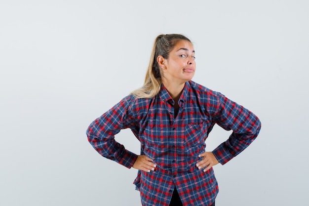 Mujer joven en camisa a cuadros cogidos de la mano en la cintura, sonriendo y mirando feliz