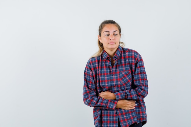 Foto gratuita mujer joven en camisa de cuadros con dolor de estómago y aspecto cansado