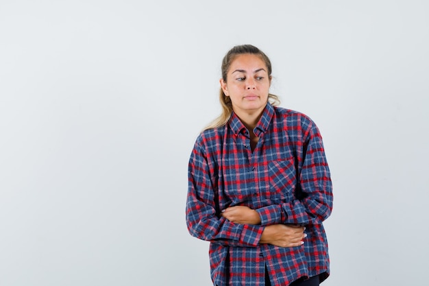 Mujer joven en camisa de cuadros con dolor de estómago y aspecto cansado
