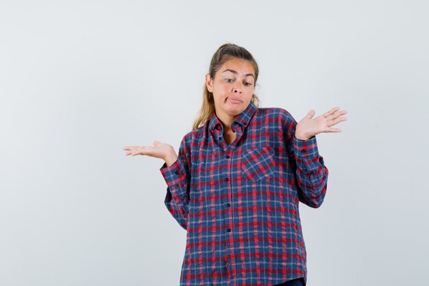 Mujer joven en camisa de cuadros encogiéndose de hombros y mirando desconcertado