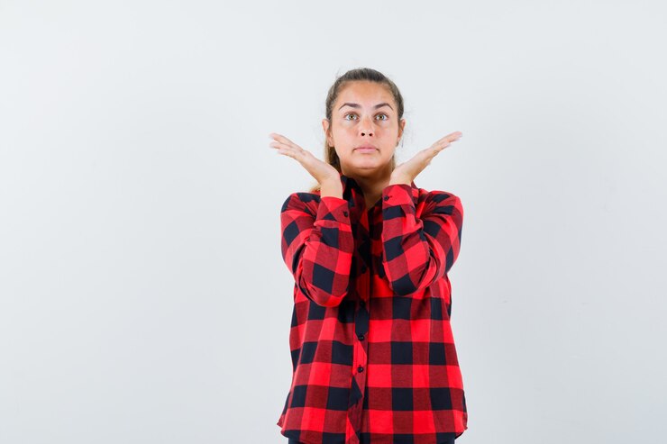 Foto gratuito mujer joven en camisa a cuadros levantando las manos mientras mira hacia arriba y mira esperanzada, vista frontal.