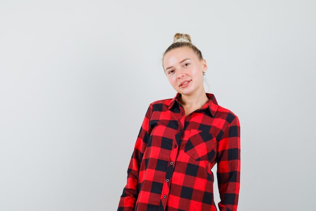 Mujer joven en camisa a cuadros mirando confiado, vista frontal.