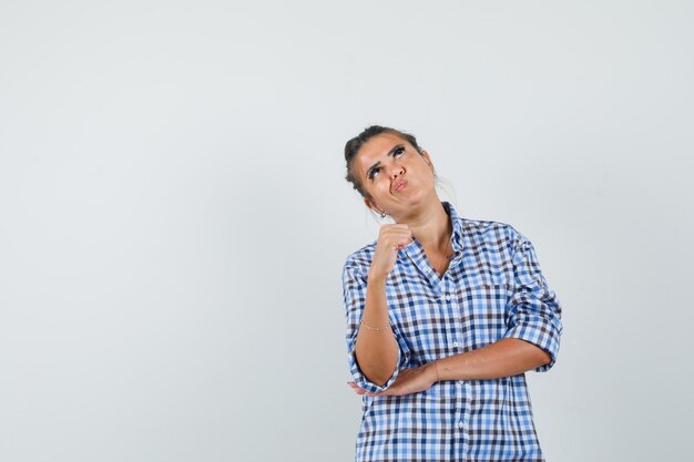 Mujer joven en camisa a cuadros pensando en algo y mirando concentrado.