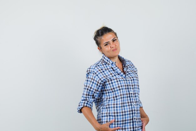 Mujer joven en camisa a cuadros posando y mirando confiada.