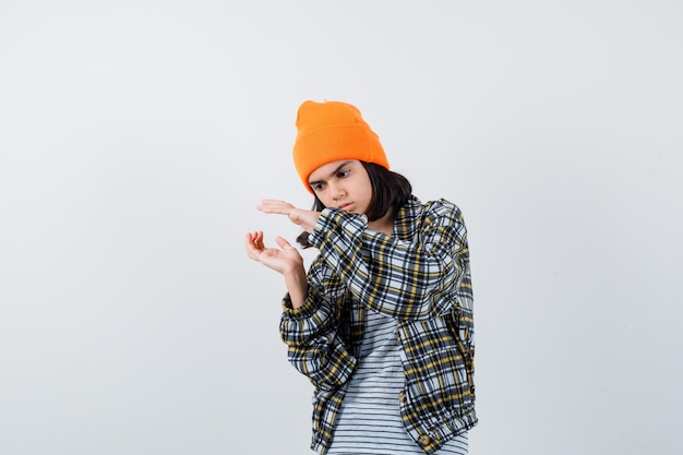 Mujer joven en camisa a cuadros sombrero naranja fingiendo sostiene algo que parece serio