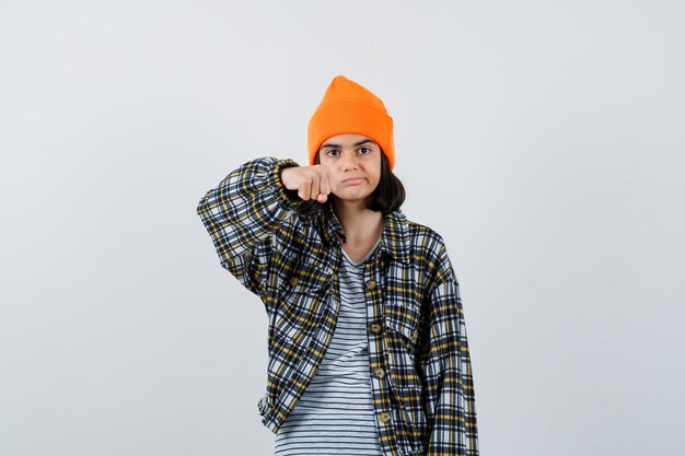 Mujer joven en camisa a cuadros sombrero naranja mostrando puño mirando disgustado