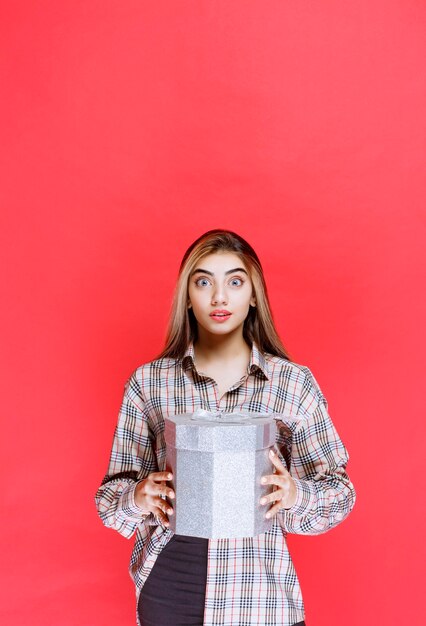 Mujer joven en camisa de cuadros sosteniendo una caja de regalo plateada