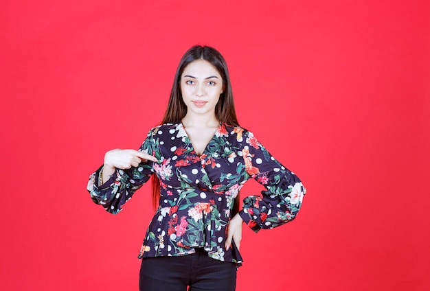 Mujer joven, en, camisa floral, posición, en, pared roja, y, presentación, ella misma