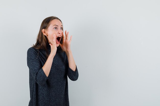 Mujer joven en camisa gritando con las manos cerca de la boca