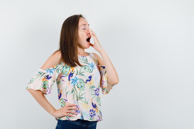 Mujer joven en camisa, jeans bostezando y mirando soñoliento, vista frontal.