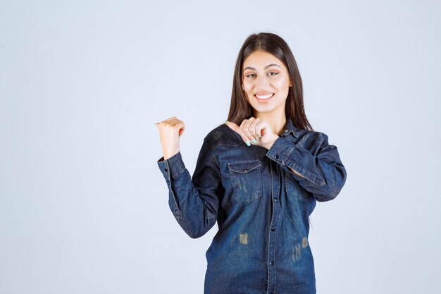 Mujer joven en camisa de mezclilla apuntando a algo detrás