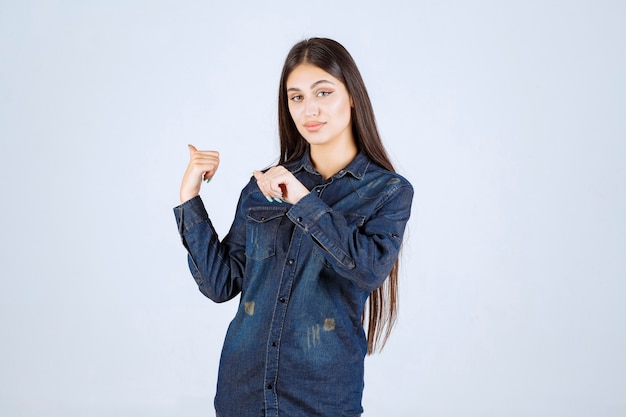 Mujer joven en camisa de mezclilla apuntando a algo detrás