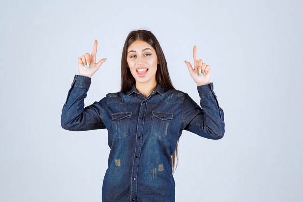 Mujer joven en camisa de mezclilla apuntando a algo en el lado positivo