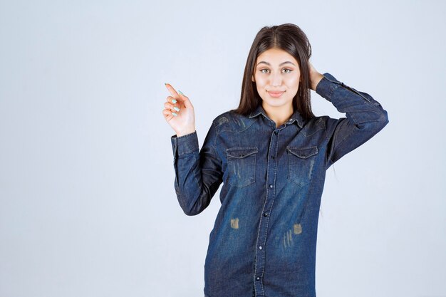 Mujer joven en camisa de mezclilla apuntando a algo en el lado positivo