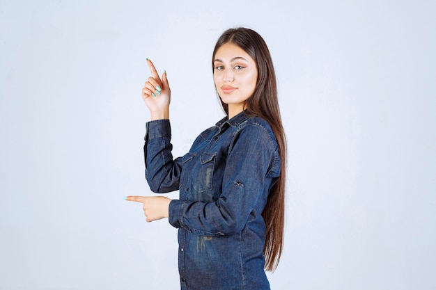 Mujer joven en camisa de mezclilla apuntando a algo en el lado positivo