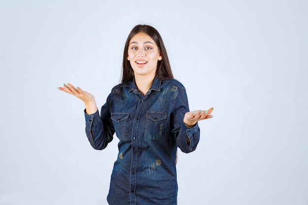 Mujer joven en camisa de mezclilla apuntando a alguien adelante e invitándolo