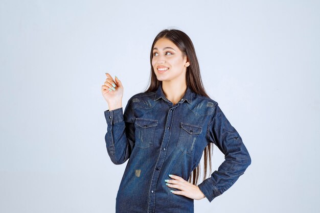 Mujer joven en una camisa de mezclilla apuntando hacia el lado izquierdo con emociones de cara