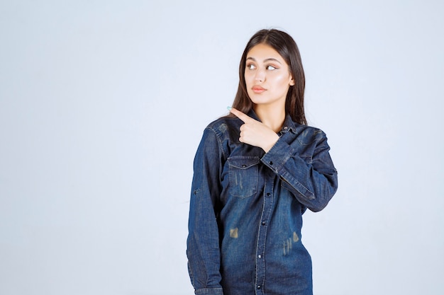 Mujer joven en camisa de mezclilla apuntando hacia el lado izquierdo