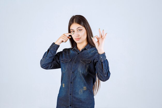 Mujer joven en camisa de mezclilla mirando a través de sus dedos