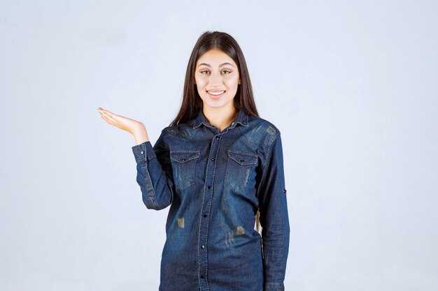 Mujer joven en camisa de mezclilla mostrando algo en su mano