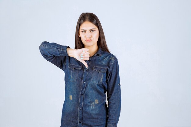 Mujer joven en camisa de mezclilla mostrando el pulgar hacia abajo