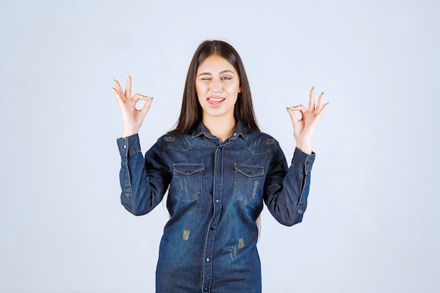 Mujer joven en camisa de mezclilla mostrando signo de disfrute