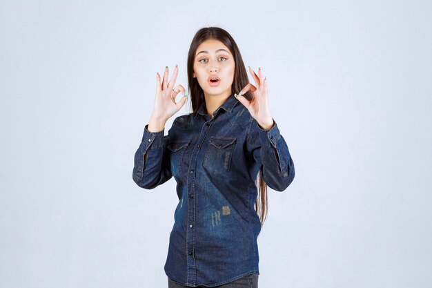 Mujer joven en camisa de mezclilla mostrando signo de mano positivo