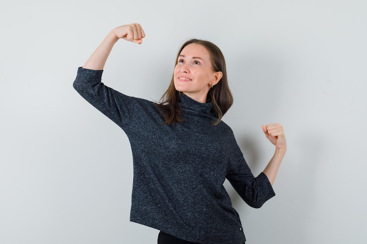 Foto gratuito mujer joven en camisa mostrando gesto de ganador y mirando soñadora