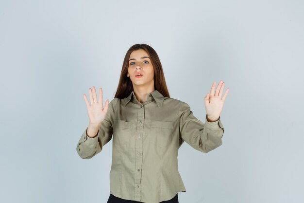 Foto gratuita mujer joven en camisa mostrando gesto de parada y mirando asustado, vista frontal.