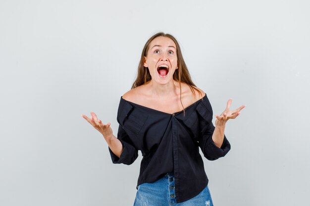 Mujer joven en camisa, pantalones cortos levantando las manos y abriendo la boca