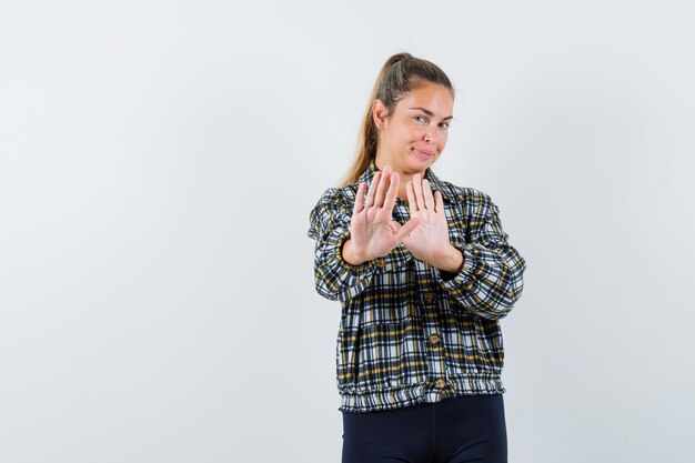 Mujer joven en camisa, pantalones cortos mostrando gesto de parada y mirando confiado, vista frontal.