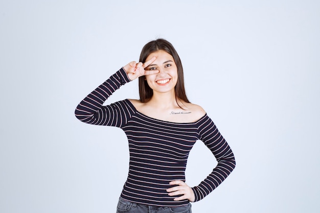 Mujer joven en camisa a rayas enviando el signo de la paz